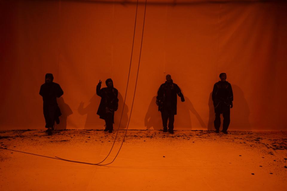 4 figures in rain suits stand in front of a wall